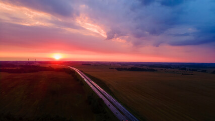 Aerial view of highway on red sunset. Landscape with road near countryside fields. Beautiful winding road leading through rural countryside with evening sunlight. Dramatic sky background.