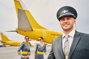 Fototapeta premium Joyous male pilot and stewardesses on the runway