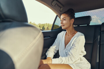 Relaxed lady sitting near window in the back of car