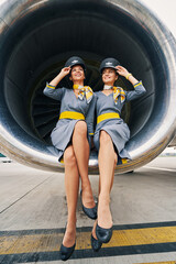 Beautiful stewardesses in uniforms sitting cross-legged inside the turbofan engine - obrazy, fototapety, plakaty