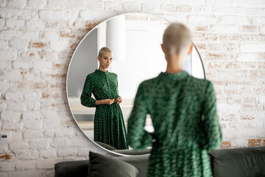 Stylish Woman In Green Dress Looks At Herselfes In The Mirror, Getting Ready To Go Out. Female Style And Beauty Concept