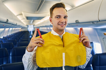 Cheerful handsome flight attendant wearing a lifejacket - obrazy, fototapety, plakaty