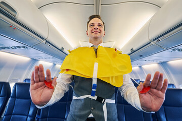 Smiling young steward inflating his the lifejacket aboard the aircraft - obrazy, fototapety, plakaty