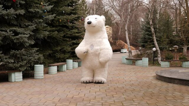 A white big bear doll with a human growth on the street of the city in winter, a holiday. A large growth bear for a birthday and new year.