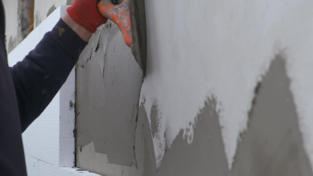 Construction worker covering house wall with adhesive cement glue berore installing styrofoam insulation sheets for thermal protection.