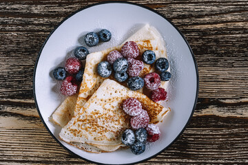 Summer dessert, crepes with berries on wooden background