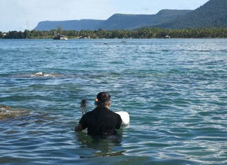 A man in a black T-shirt catches sea urchins while standing in the sea up to his chest