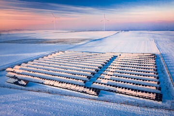 Snowy solar panels and wind turbines in winter at sunrise.