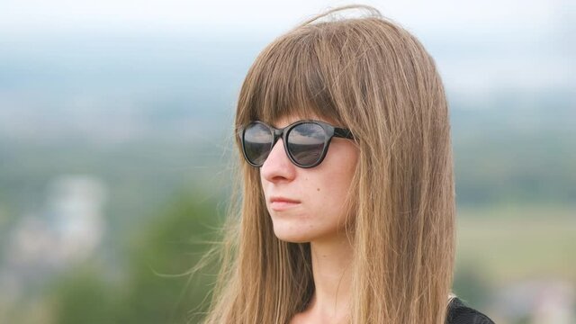 Portrait of a young long haired woman in dark sunglasses relaxing outdoors on a windy summer day.