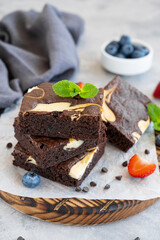 Delicious chocolate brownie cheesecake with fresh berries and mint on a wooden board on a gray concrete background. Copy space.