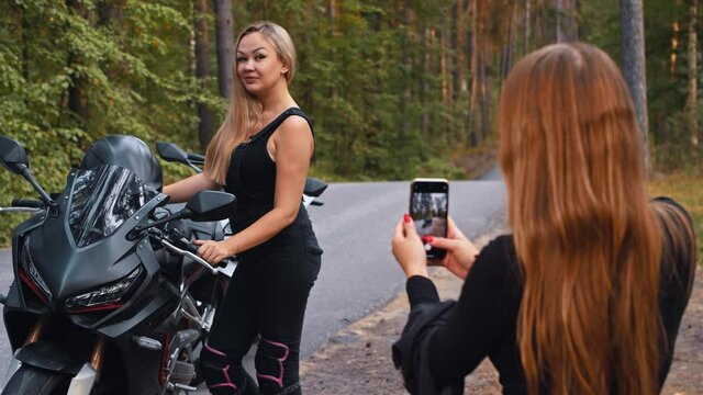 Smiling women friends taking photos on motorbikes in the forest - blonde woman posing