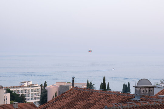View of a distant parasailer flying over the see and rooftops of Becici, Montenegro against a colorful sky