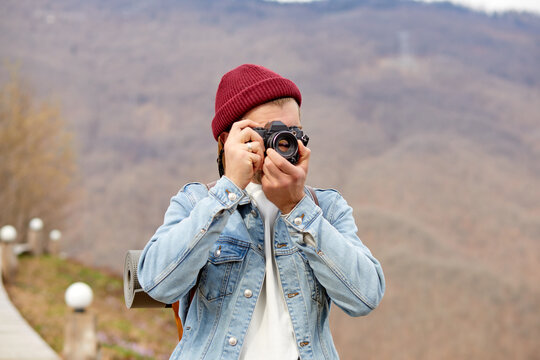 Young Man Traveler at vacations in mountains, take photo of nature. Lifestyle hiking concept. Portrait of hipster guy in denim jacket and hat using camera, enjoy traveling alone