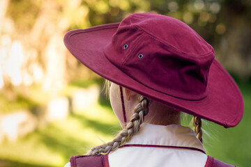 A girl wearing school uniform, white shirt, maroon backpack and a hat Back to school. Return to classrooms after COVID-19 outbreak in Australia