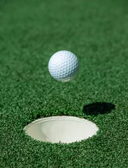Poster An golf ball about to fall into the hole of a green.  Hole in one image. © Jurie