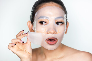 A beautiful Asian woman peeling a collagen face mask. Skincare concept, anti-aging moisturizing...