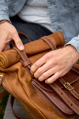 Fototapeta premium Unrecognizable Male hands opening leather brown backpack, style and fashion concept. outdoors close-up photo. leather accessory, handmade backpack