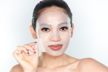 A beautiful Asian woman peeling a collagen face mask. Skincare concept, anti-aging moisturizing...