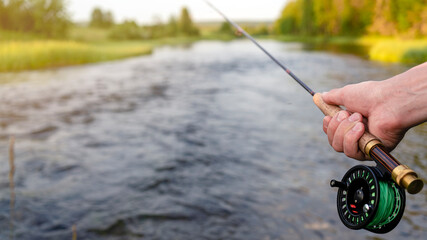 Fly fishing rod in fisherman hand. Fishing on the mountain river. Summer Activities.