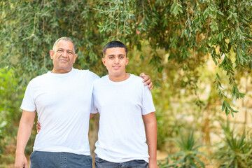 Teenager son and senior father standing outdoors. Old father hugging young teen son against nature background.