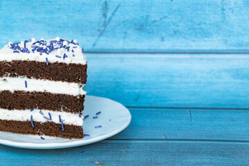 A piece of chocolate sponge cake with a layer of butter cream located on the left. Purple sprinkles. Blue background.