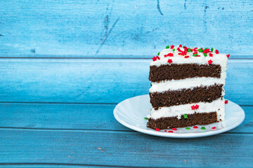 A piece of chocolate sponge cake with a layer of butter cream located on the right. Blue background. Red-green dusting