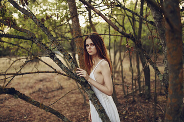 Naklejka premium pretty woman in white dress near trees fallen leaves in the forest