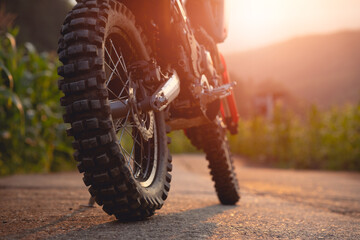 Part of a dirt bike on a dirt road in a cornfield with warm light. Copy space.