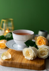 A cup of herbal tea and a bouquet of roses on a green background. Warm and pastel tones. Top view. Still life
