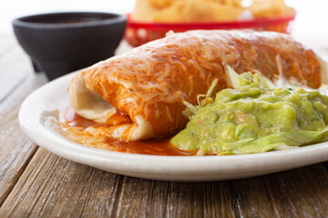 A view of a wet burrito, with a side of guacamole.