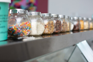 A view of several jars of a variety of dessert toppings, seen at a local ice cream store.