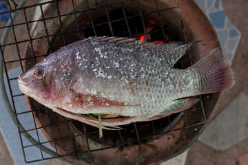 Top view of Grilled tilapia with salt on iron grate vintage charcoal stove.