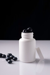 blueberry pills in white bottle on white table and black background