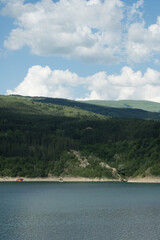 Beautiful Zavojsko jezero (Zavoj lake) view over the wavy water with sunlit mountains and green forests on the other side and rafts in the water