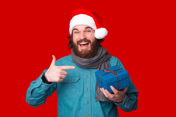 Cheerful young man is pointing at a blue gift he is holding.