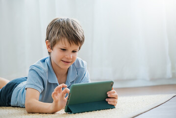 Portrait of little boy looking at tablet computer playing with digital tablet at home, little caucasian boy using laptop. Weekend holiday leisure time education, online home school quarantine concept