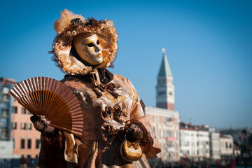 Female wearing a mask, hat and carnival costume holding a fan in her hand in Venice, Italy