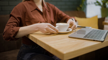 Close-up of young woman drinking cup of coffee in restaurant, freelancer taking a break