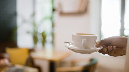 Male waiter serving cup of coffee to customer's table in cafe, service, close-up