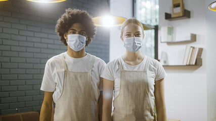 Male and female waiters wearing face masks in restaurant, safety during pandemic, portrait