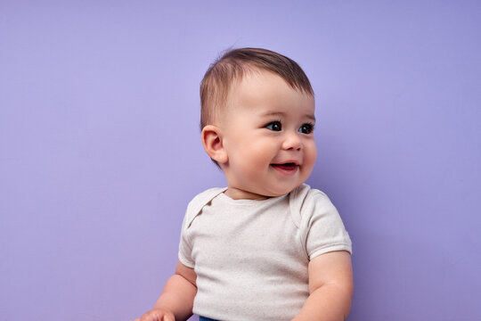 child is smiling enjoying adopted life. Concept of happy family or successful adoption or parenting. Little baby in casual wear looking at side enjoying, sweet child isolated over purple background