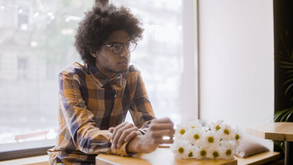 Mixed race man with afro hair sitting in cafe alone, flowers on table, waiting for date