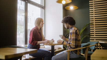 Mixed-race male and female friends drinking coffee together and talking in cafe