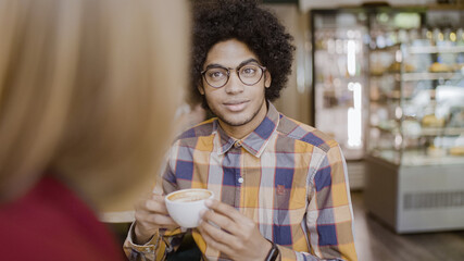 Smiling young man with afro hair enjoying coffee and talking to female friend in cafe