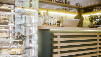 Large variety of desserts on glass stand in bakery shop, business, female barista cleaning shelves