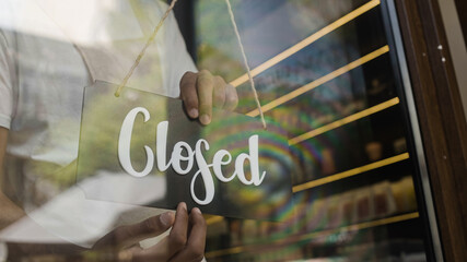 Male shop worker putting closed door sign on, end of work day, economic crisis