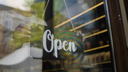 Female shop employee putting open door sign on, new work day, starting business