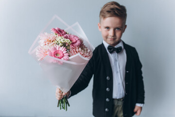 Cute adorable boy in suit with bouquet of fresh flowers. Little cheerful gentelman