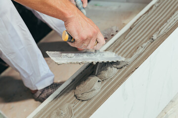 Male worker professional mounts ceramic tile in bathroom photo with close spatula with glue