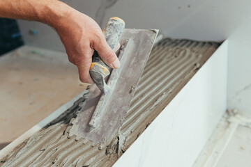 Male worker professional mounts ceramic tile in bathroom photo with close spatula with glue